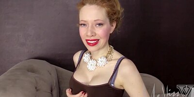 Ginger woman with red lips is slowly taking off her clothes in front of the camera